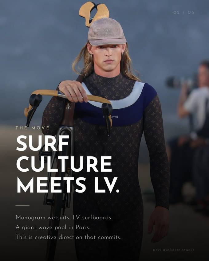 A model on a sandy Paris runway wearing a Louis Vuitton monogram wetsuit and cap, holding a road bike, with a camera operator visible in the background.